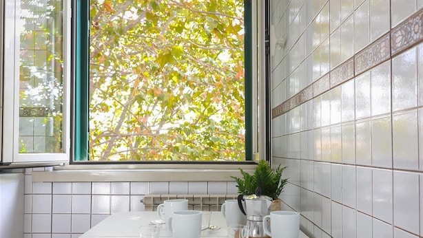 A kitchen with white tiles, a window with a view of trees, and a coffee maker on the counter. - Bright apartment in Via Ginori, in the heart of the Testaccio district (Rome)