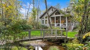 A house with a covered porch, a wooden bridge, and a small stream.