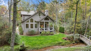 A cabin with a porch, surrounded by a well-maintained lawn and a small stream.