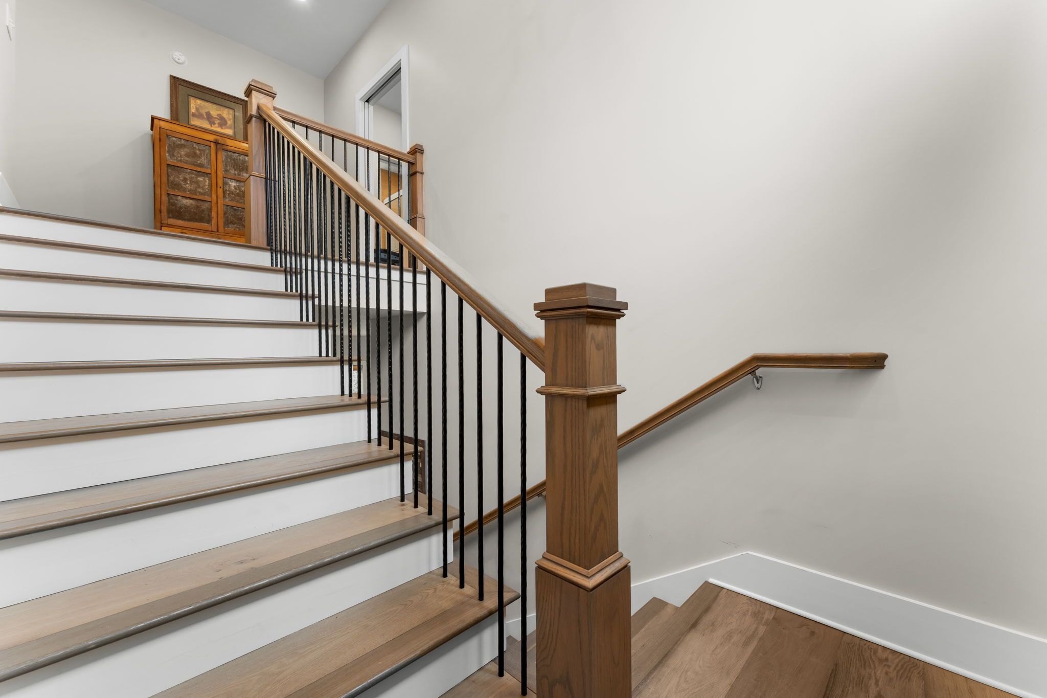 A staircase with wooden steps and black railings, leading to a landing with a door and a framed picture.
