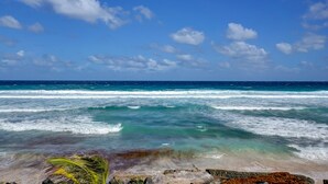 A beach with clear blue sky, ocean waves, and rocky shoreline.