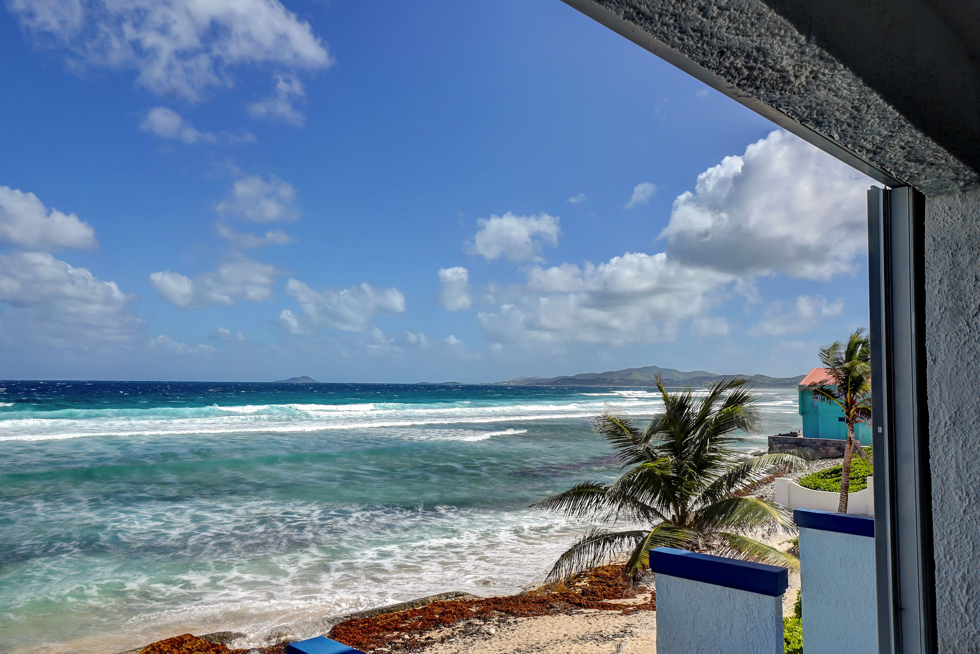 Blick auf den Ozean von einem Balkon, mit blauem Himmel und einer entfernten Bergkette.