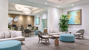 Un área de recepción moderna con zona de estar, mostrador de recepción y una planta grande.