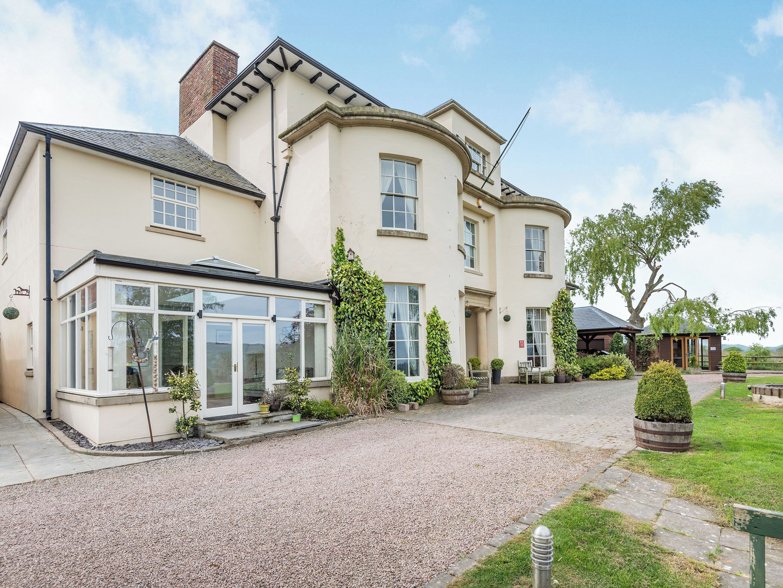 A large, two-story building with a conservatory, a gravel driveway, and a well-maintained garden.