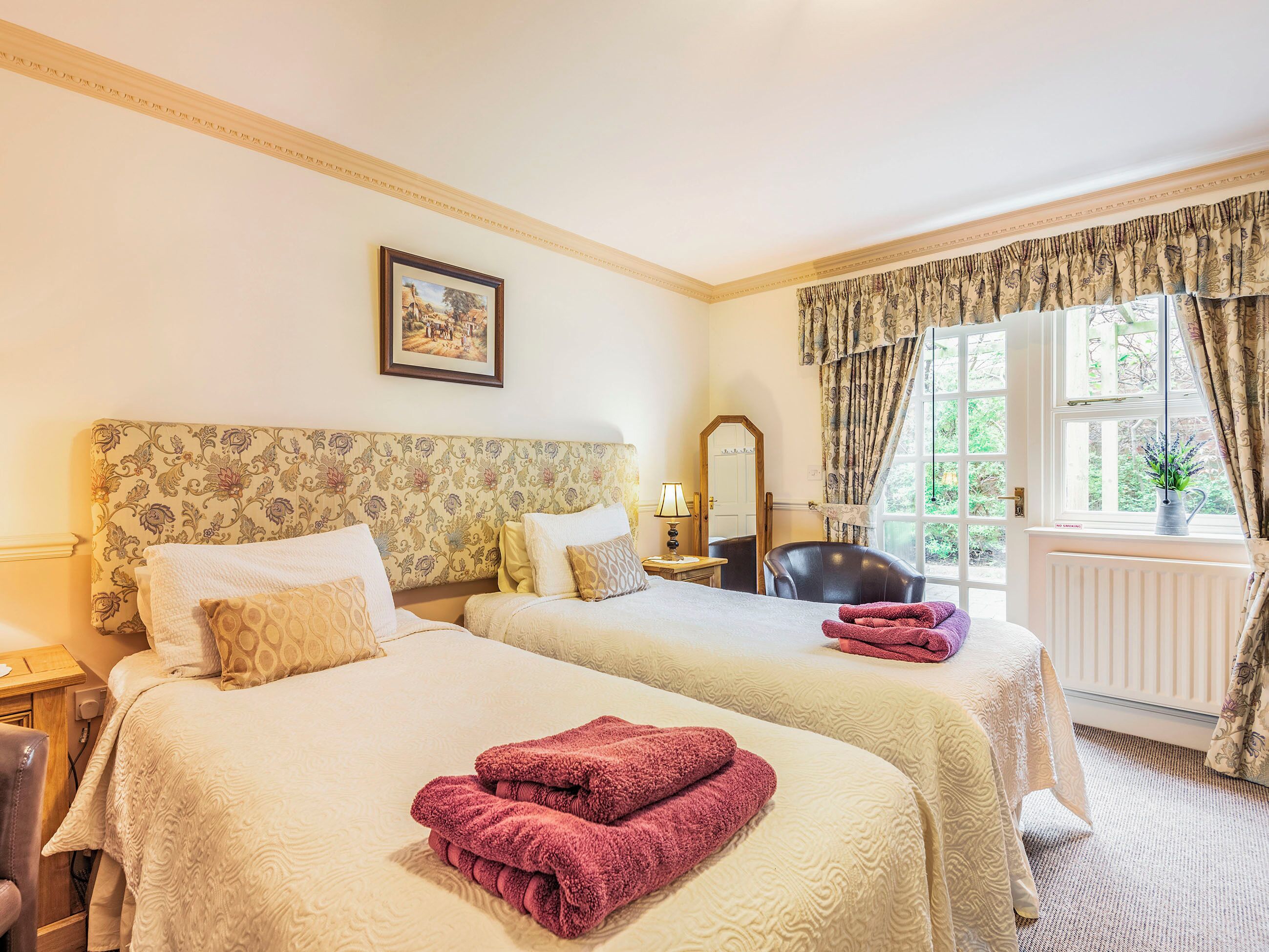 Une chambre d’hôtel avec deux lits, un coin salon, une fenêtre avec des rideaux et un tableau encadré au mur.