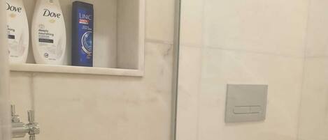A bathroom with a toilet, a shower, and a shelf with Dove and Clinique products.