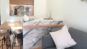 A modern kitchen with marble countertops, a built-in oven, and a sink. There is a bar area with stools and a grey sofa with a white pillow. - Principe Real Central Home - Free Airport Transfer (Lisboa)