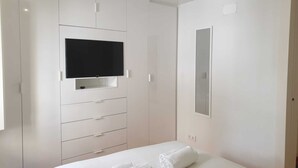 A modern hotel room with a bed, a flat-screen TV mounted on a white wardrobe, and a mirror on the wall. - Principe Real Central Home - Free Airport Transfer (Lisboa)