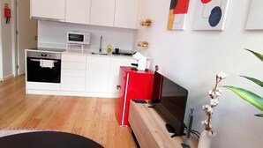 Uma cozinha moderna com armários brancos, micro-ondas e bancada vermelha.
