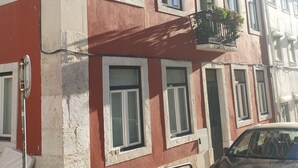 Um edifício de vários andares com paredes externas em vermelho e branco, diversas janelas com molduras brancas e varandas com grades pretas.