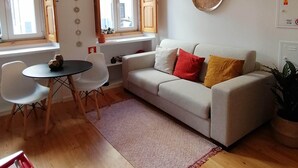 Uma sala de estar com sofá, duas cadeiras, uma mesa pequena e uma janela com persianas de madeira.