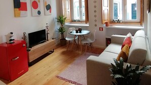 Uma sala de estar moderna com um armário vermelho, uma TV, um sofá e um espaço de jantar com mesa e cadeiras.
