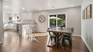 A spacious kitchen with white cabinets, a large island, and a dining area with a wooden table and chairs. - BA's BohoChic-steps to Rose District w/Hot Tub (Broken Arrow)