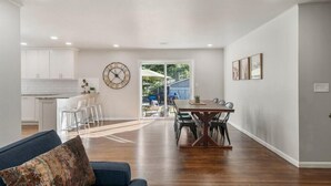 A spacious living area with a dining table and chairs, a sofa, and a kitchen in the background. - BA's BohoChic-steps to Rose District w/Hot Tub (Broken Arrow)
