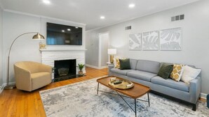 A living room with a fireplace, a sofa, a coffee table, and a floor lamp. - Ranch Acres Expo-Heart of Tulsa (Tulsa)
