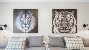 A hotel room with two beds, each with a grey bedspread and a plaid pillow. There are two wall-mounted paintings, one of a lion and one of a tiger. - Ranch Acres Expo-Heart of Tulsa (Tulsa)