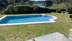Une piscine rectangulaire à bord incurvé, entourée d’une pelouse bien entretenue et d’une végétation dense.