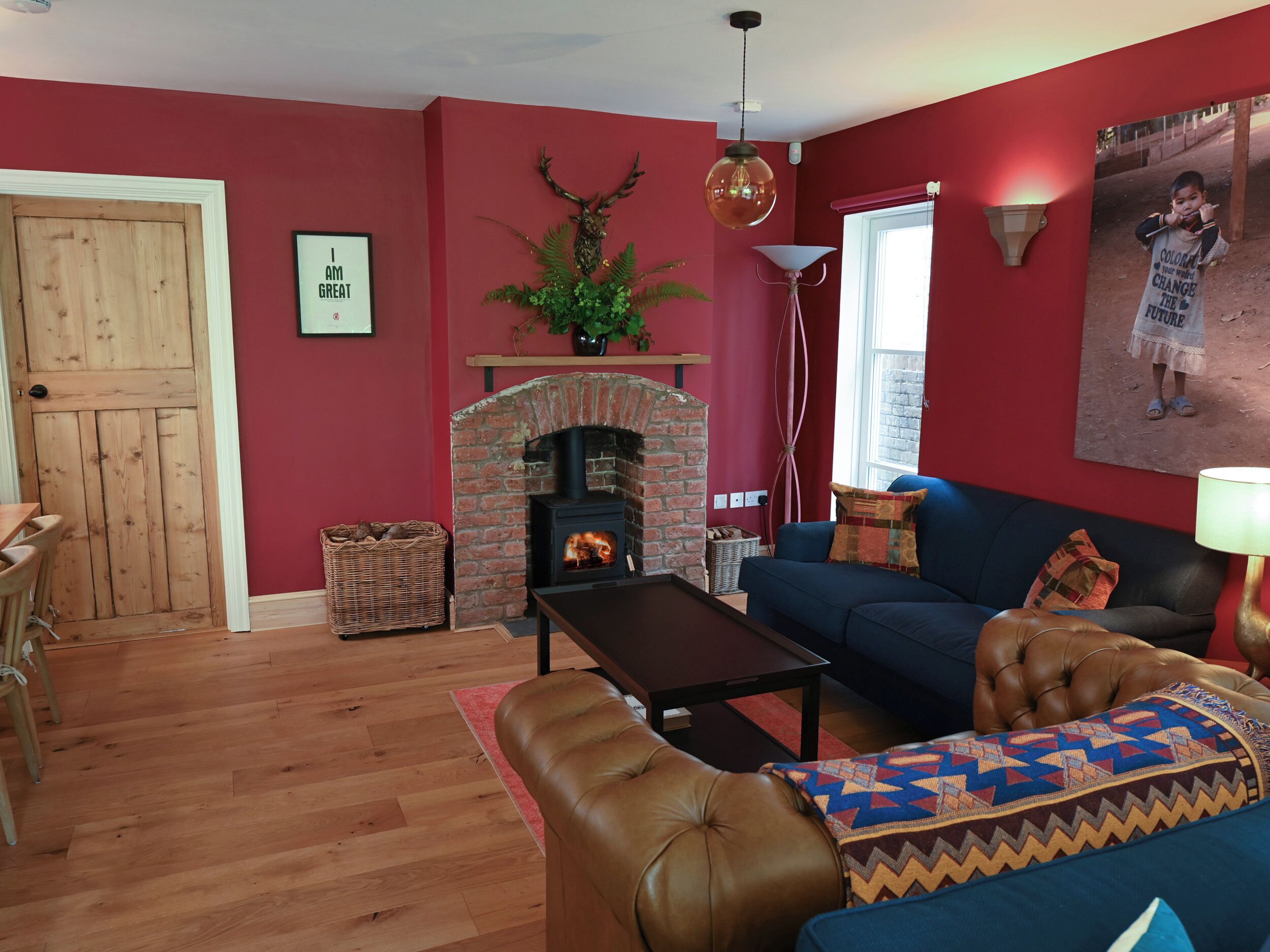 A living room with a brick fireplace, a blue sofa, a brown leather couch, and a wooden door.