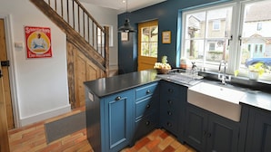 A kitchen with blue cabinets, a wooden staircase, and a window with a view of the outside. - Gingerbread Cottage (Canterbury)
