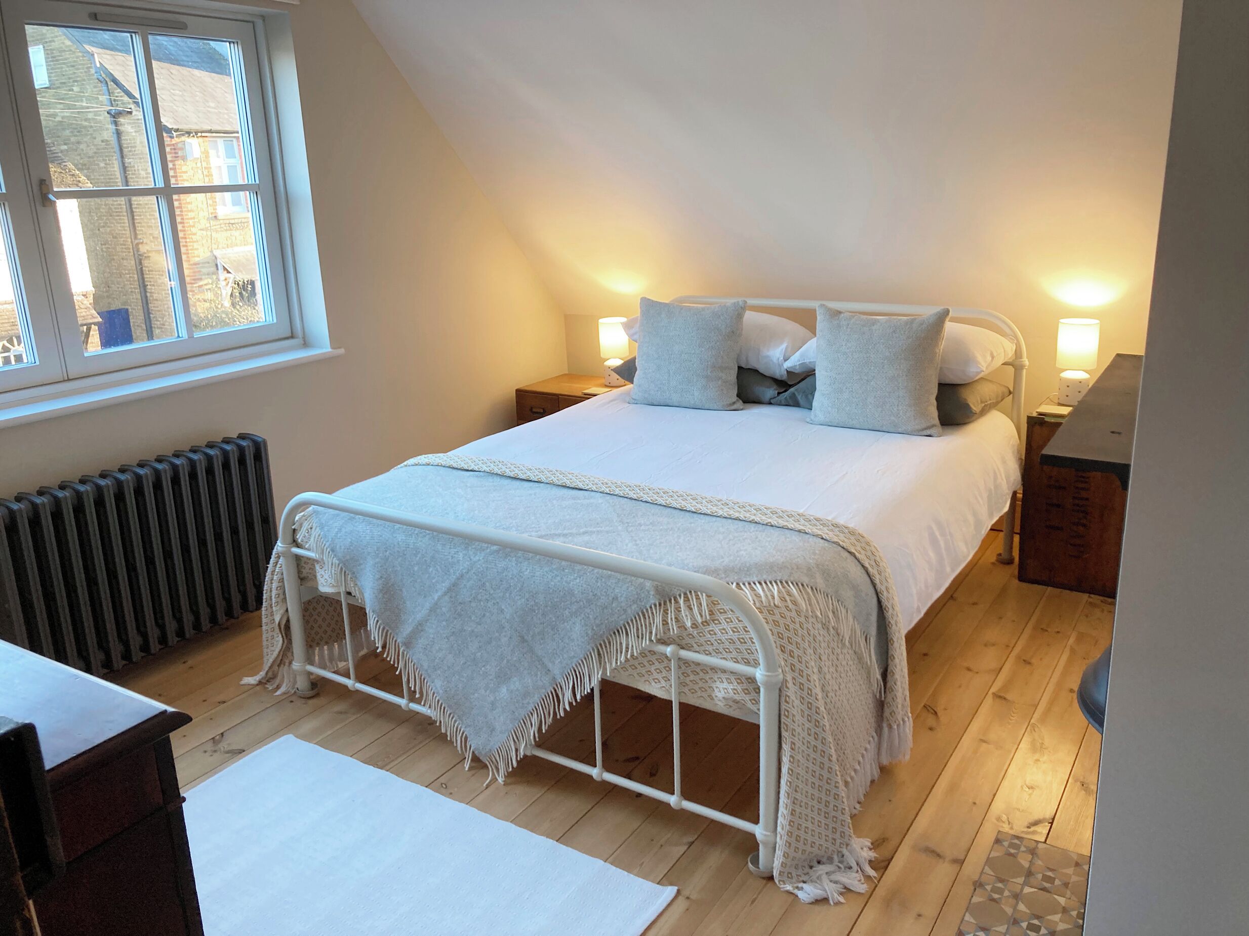 A cozy bedroom with a bed, bedside lamps, a radiator, and a window.