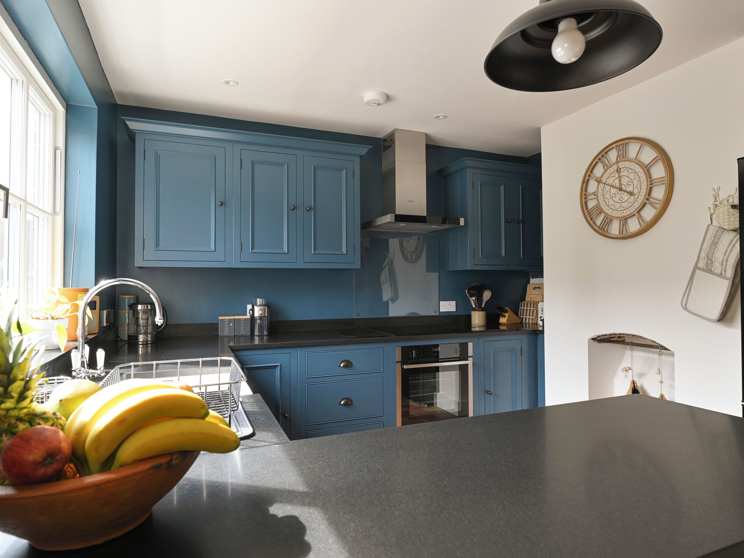 A kitchen with blue cabinets, a black countertop, and a fruit bowl with bananas and apples.