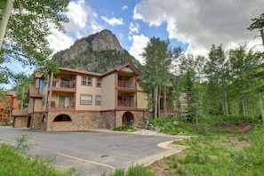 A multi-story building with a stone facade, multiple balconies, and a view of a mountain.