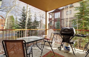 A balcony with a glass table and chairs, a barbecue grill, and a propane tank.