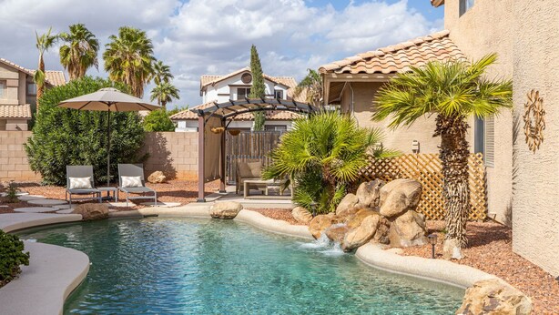 A swimming pool with a waterfall feature, surrounded by palm trees and lounge chairs. - Perfect Family Haven: 5BR,Heated Pool + Golf Green (Gilbert)