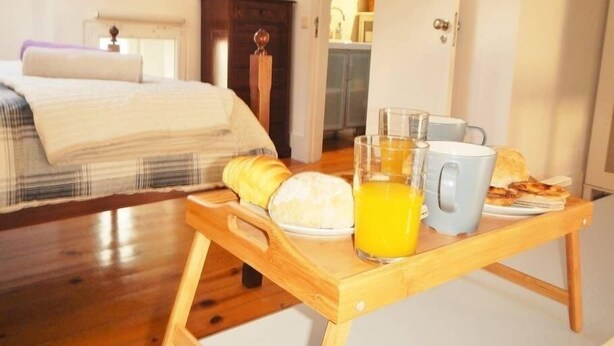 Quarto com uma cama, mesa de cabeceira de madeira e bandeja de café da manhã com suco de laranja e pão.