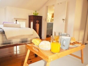 Une chambre à coucher avec un lit, une table de chevet en bois et un plateau de petit-déjeuner avec du jus d’orange et du pain.