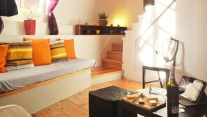 Uma sala de estar aconchegante, com um sofá, uma mesinha com uma garrafa e copos, e uma escada que leva a outro andar.