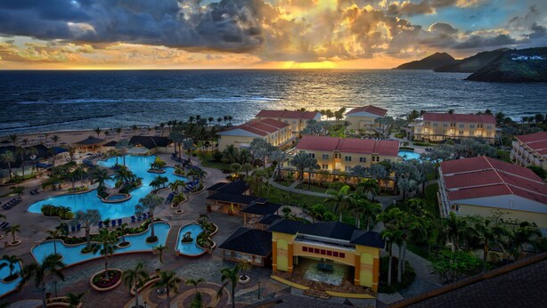 Un complexe hôtelier doté de plusieurs piscines, d’une grande piscine centrale et offrant une vue sur l’océan au coucher du soleil.