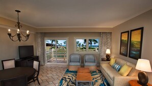 Une chambre d’hôtel comprenant un coin repas, un ensemble de canapés, une télévision et une vue sur la plage, accessible par des portes coulissantes.