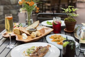 A dining table with various dishes, including bread, a salad, and a meat dish, along with drinks and a potted plant.