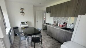 A modern kitchen with grey cabinets, a black countertop, and a white refrigerator. There is a dining table with two chairs and a microwave on the countertop.