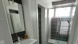 A modern bathroom with a white vanity, a large mirror, and a shower area.