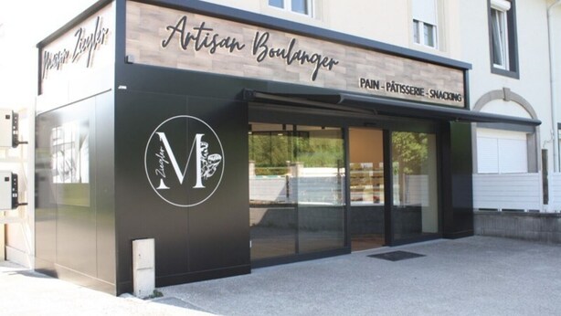 A storefront with a sign reading "Artisan Boulanger" and "Pain - Pâtisserie - Snacking".