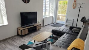 A modern living room with a large flat-screen TV, a sofa, a coffee table, and a patterned rug.