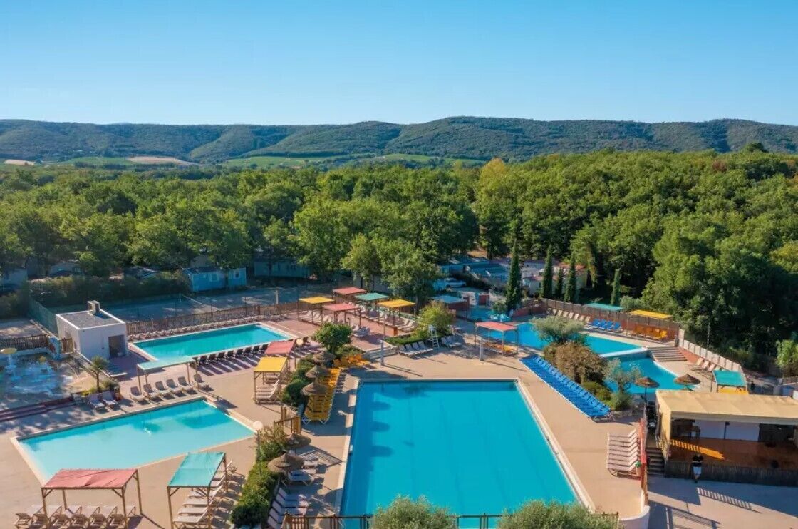 A resort with multiple swimming pools, sun loungers, and umbrellas, surrounded by lush greenery and hills.