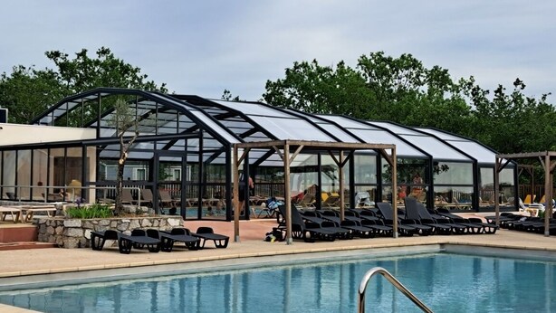 A swimming pool with lounge chairs and a glass-enclosed structure. - NEW AIR CONDITIONED MOBIL HOME - CAMPING 5* - FOR 6 PEOPLE with dishwasher (Lagorce)