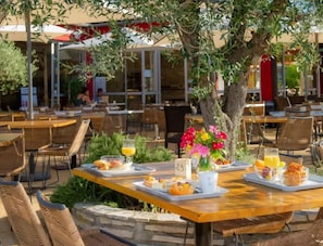 Un espace extérieur aménagé pour les repas, avec des tables, des chaises et un arbre.