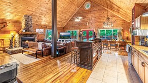 A spacious log cabin interior with a fireplace, wooden floors, a dining area, and a kitchen. - Smoky Mountain Cabin | Hot Tub + Pool Table (Sevierville)