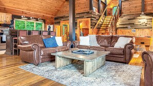 A cozy cabin interior with a wooden ceiling, leather sofas, a dining area, and a staircase. - Smoky Mountain Cabin | Hot Tub + Pool Table (Sevierville)