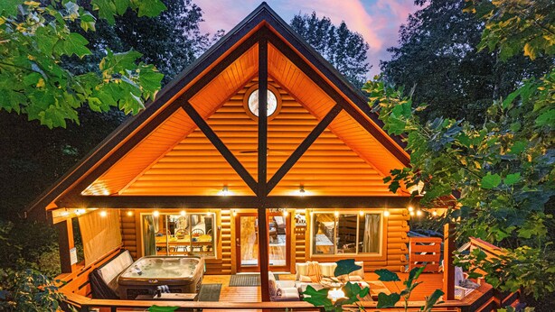 A log cabin with a hot tub, outdoor seating, and a deck surrounded by foliage. - Smoky Mountain Cabin | Hot Tub + Pool Table (Sevierville)
