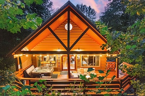 A log cabin with a hot tub, outdoor seating, and a deck surrounded by foliage. - Smoky Mountain Cabin | Hot Tub + Pool Table (Sevierville)