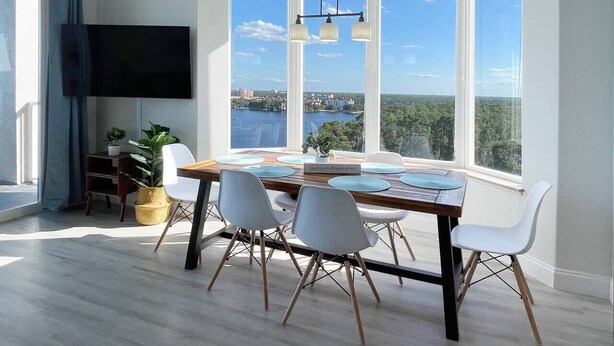 Un comedor con una mesa grande, sillas blancas y vistas al mar a través de amplios ventanales.
