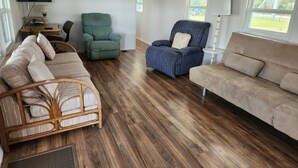 Een moderne woonkamer met een houten vloer, een flatscreen televisie aan de muur, een groene fauteuil, een blauwe fauteuil en een beige bank.
