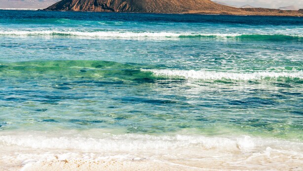 Uma praia com águas turquesa cristalinas e uma montanha ao longe.
