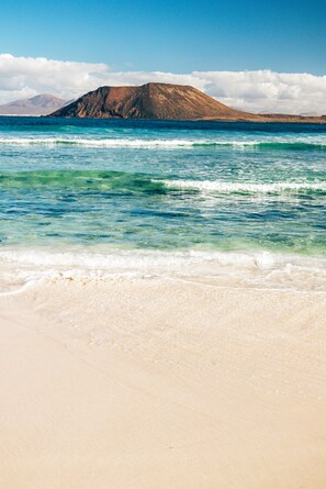 A beach with clear turquoise water and a distant mountain. - Accommodations with a spa. Free Wi-Fi. 0.3 km from the beach. We accept children over the age of 12 (Corralejo)