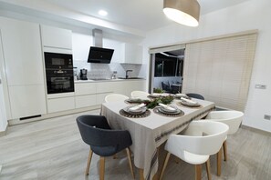 A modern kitchen with white cabinets, a built-in oven, and a flat-screen TV.